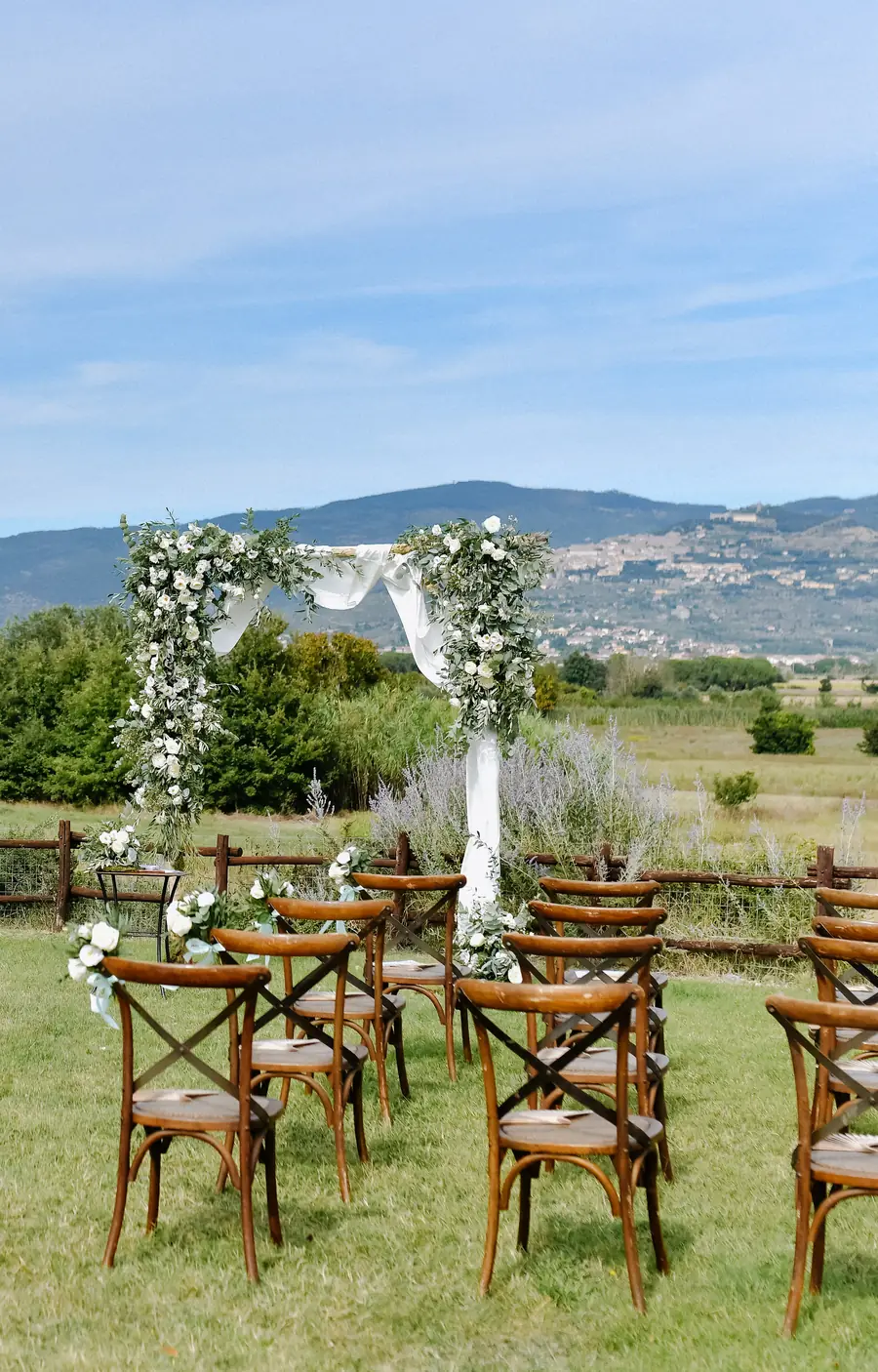Le sedie di legno e l'arco di fiori bianchi sul prato, davanti alle colline
